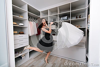 Enthusiastic young woman jumping in dressing room, nice wardrobe with skirt in hands. She`s happy with the choice. She`s Stock Photo