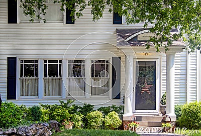 Entrance of charming white wood house with columns on porch and beautiful landscaping and overhanging branches and a red white and Stock Photo