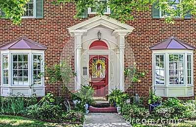 Entrance with columns and bay windows of beautiful two-story brick house with pots of flowers and yellow climbing roses and Stock Photo