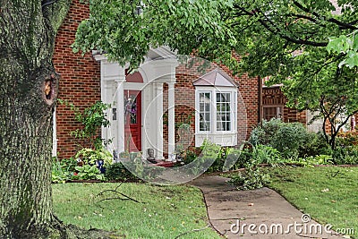 Entrance of nice brick house with bay windows after a storm that left branches and leaves littered over sidewalk and yard Stock Photo