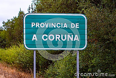 Entrance road sign of province of A Coruna on green background by dense trees in Spain Editorial Stock Photo