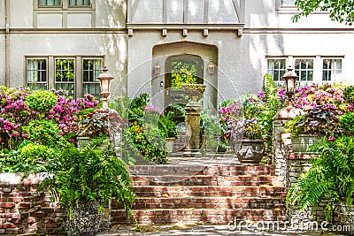 Entrance to up-scale chalet-like stucco house with brick stairs up to flower filled courtyard with fountain and trees reflected in Stock Photo