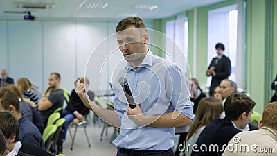 Entraîneur professionnel dans la chemise bleue parlant dans le microphone et gesticulant à l'atelier pour futurs directeur généra banque de vidéos Entraîneur professionnel dans la chemise bleue parlant dans le microphone et gesticulant à l'atelier pour futurs directeur généra banque de vidéos