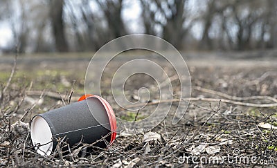 Enviromental pollution; paper cup for coffee and red plastic cover on a background of forest nature and grass. Stock Photo