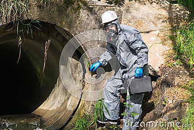 An environmental laboratory specialist in a protective suit and mask holds a case with a mobile laboratory in his hands and goes Stock Photo