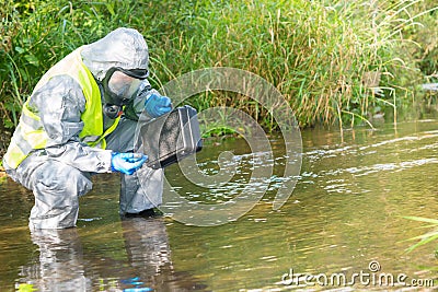 An environmental laboratory specialist in a protective suit and mask stands in the water and measures the level of pollution with Stock Photo