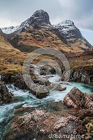 Epic landscape image of vibrant River Coe flowing beneath snowcapped mountains in Scottish Highlands Stock Photo