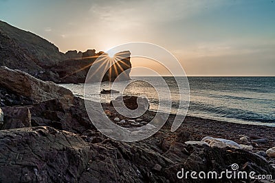 An epic sunset on the sea - the sun sets behind the mountain and everything shines with warm light with long rays. Stock Photo