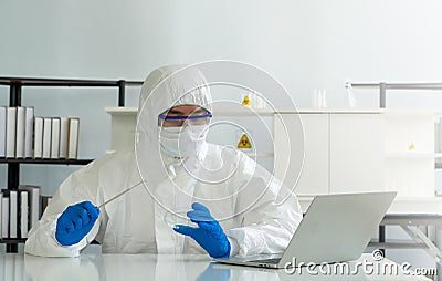 Epidemiological researchers in virus protective clothing look at laptop computer screen while holding Inoculating Needle and Stock Photo