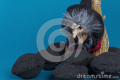 Epiphany holiday concept. Witch Befana and coal pieces for naughty kids on blue background. Stock Photo