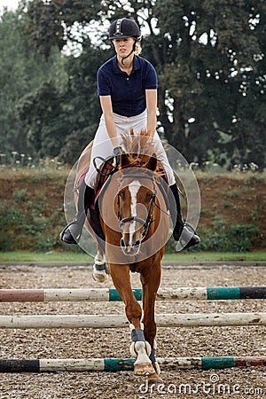 Bay horse with jockey girl jumping over a hurdle. A horse and rider in jump motion, in the air, equestrian competition in the rain Stock Photo