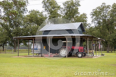 Equipment for agriculture and recreation sits under the shed roof of a painted wooden barn in a pecan orchard in rural Georgia Editorial Stock Photo
