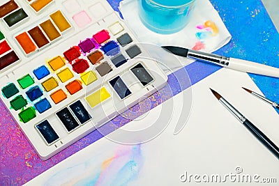 Equipment for painting, the bright palette of watercolors, some brushes, water bowl and paper for drawing Stock Photo