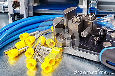 Equipment for wiring close-up. Unused yellow cord end insulated ferrules with wire stripper and blue stranded wire lying on metal Stock Photo