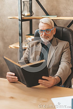 Erudite with a book. A mature student reads an encyclopedia, learning in old age. Professor in the library Stock Photo