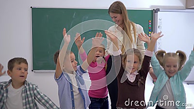Escola primária, grupo de mãos de salto e de ondulação do divertimento das crianças próximo ao professor no fundo da placa Escola primária, grupo de mãos de salto e de ondulação do divertimento das crianças próximo ao professor no fundo da placa