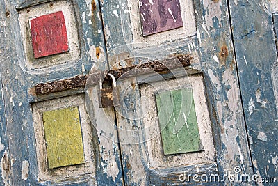 Brightly coloured flaky painted old window shutters secured with a rusting bolt and padlock- Dutch tilt Stock Photo