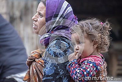 A homeless beggar woman walks through town with a young girl child carried on her back Editorial Stock Photo