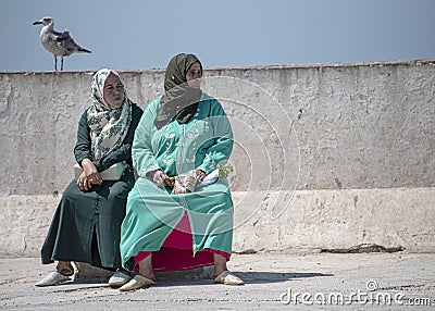 Mother and daughter, dressed in abaya and hijab, take a seat along the harbour front Editorial Stock Photo