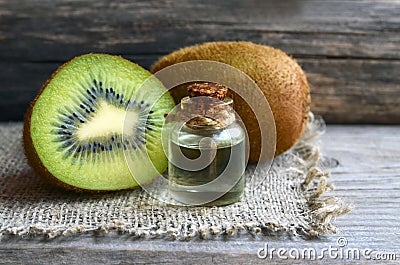 Essential kiwi seed oil in a glass jar with fresh kiwifruit whole and half on old wooden background.Aromatherapy,spa,beauty treatm Stock Photo