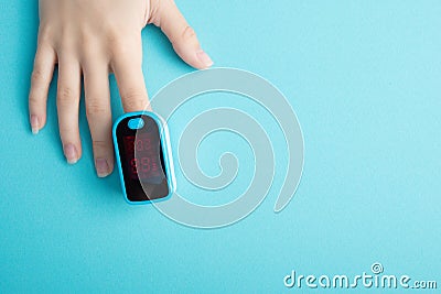 An essential medical device for hypoxia. Female finger in a pulse oximeter on a blue background with copyspace Stock Photo