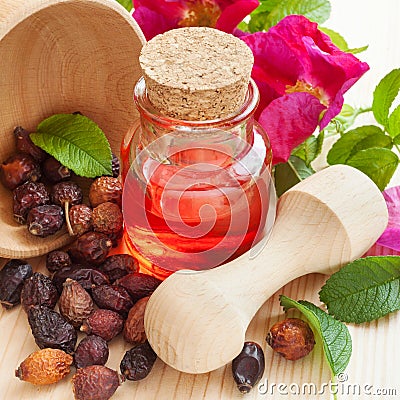 Essential oil in glass bottle, dried rose-hip berries in wooden Stock Photo