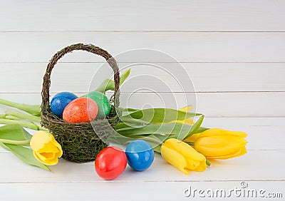 Ester eggs in basket and yellow tulips on white wooden background Stock Photo