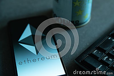 The Ethereum cryptocurrency logo is seen on the display of a smartphone on a desk with a keyboard and the symbol of Euro in the ba Editorial Stock Photo