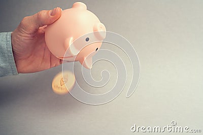 Bitcoin selling concept. Piggy bank for bitcoins. Cryptocurrency sell symbol. A man shake out bitcoin from money box on a gray bac Stock Photo