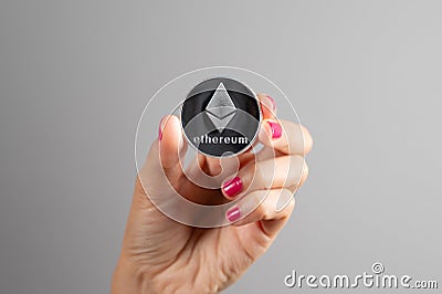 Ethereum silver coin in a woman& x27;s hand over gray background. Blockchain Cryptocurrency. Virtual Money.Crypto currency Editorial Stock Photo