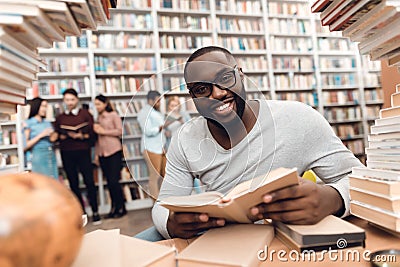 Ethnic african american guy surrounded by books in library. Student is reading book. Stock Photo