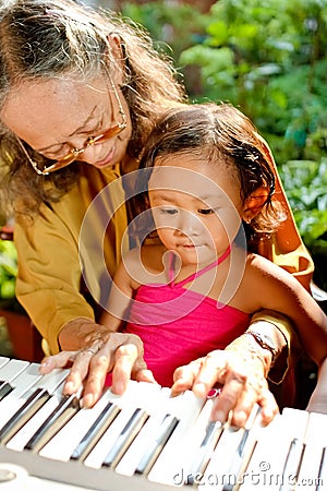 Ethnic elderly woman teach child play piano Stock Photo