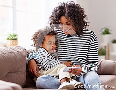 Ethnic mother and son using smartphone on sofa Stock Photo