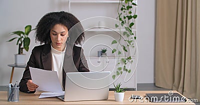 Etnische student afro - amerikaans meisje met een gekrulde achtergrond die thuis aan tafel zit , kijkt naar laptop en documentenon stock videobeelden Etnische student afro - amerikaans meisje met een gekrulde achtergrond die thuis aan tafel zit , kijkt naar laptop en documentenon stock videobeelden