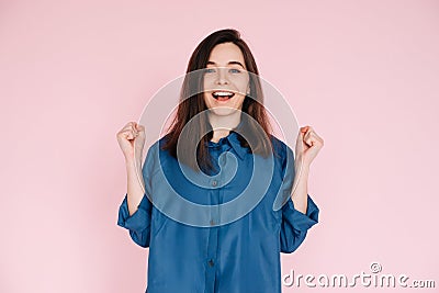 Euphoric Woman Celebrating Success, Raising Fists in Triumph: Isolated Pink Background Portrait. Joyful Woman Stock Photo