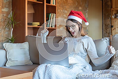 Euphoric woman smiling with arms outstretched glasses and Santa hat sitting on the sofa at home Stock Photo