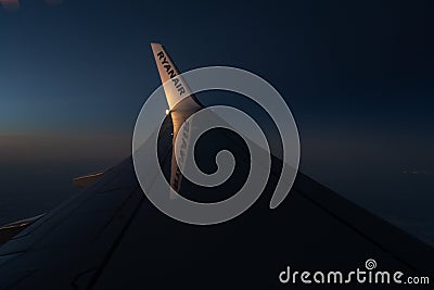 View through an airplane window onto the wing of an Ryanair Boeing 737-800 airplane with winglets in flight during sunset Editorial Stock Photo