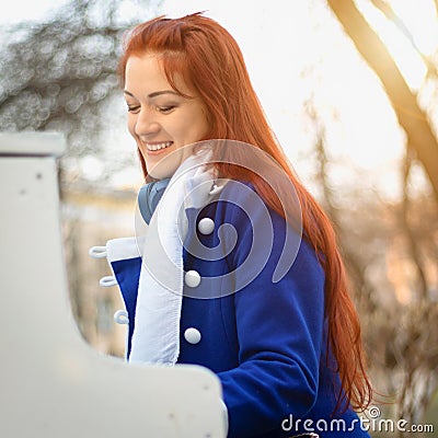 European Caucasian girl women with red hair smiles and plays the piano in the park at sunset. Modern and classical music Stock Photo