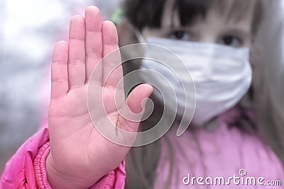 European child girl in a protective mask holds her palm in front of her, making a stop sign. Focus on the palm Stock Photo