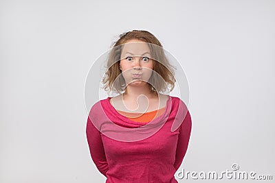 European female in pink sweater blowing her cheeks, making big wide opened eyes, frowning Stock Photo