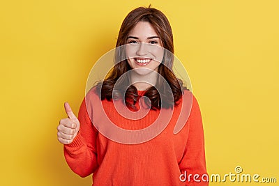 European happy young woman wearing orange clothes holds finger up shows like with thumb up isolated over yellow background girl Stock Photo