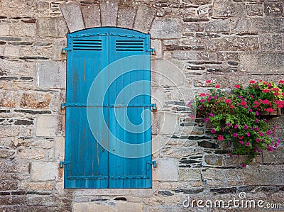 European old stone house facade with closed turquoise sun blinds window with flower pots Stock Photo