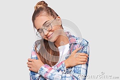 European pleased young woman dressed in casual outfit, wearing round transparent eyewear with pleasant smile, with closed eyes, Stock Photo