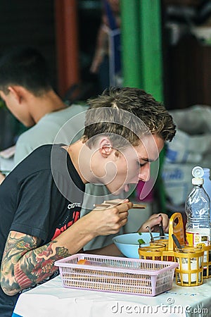 European tourist eating in street food cafe, side view. Travel around Asia. Editorial Stock Photo