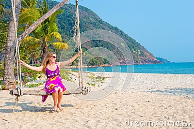 European woman, long-haired blonde in a bright dress swinging on a swing on the seashore. Travel and tourism in Asia Stock Photo