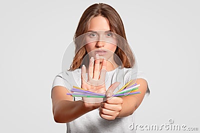 European woman with serious expression, holds plastic straws, says no to disposable plastic drinking straws in favour of metallic, Stock Photo