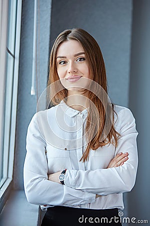 European woman is standing by the window, arms crossed and smiling. Stock Photo