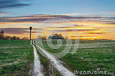 Evening sky at sunset road in the field leading to the shed barn and water tower of the rural landscape of the village. Stock Photo