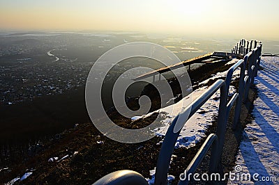 Evening view on cityscape from viewpoint hill with steel rail and old bench during snowy season. Location Nitra city, Slovakia Stock Photo