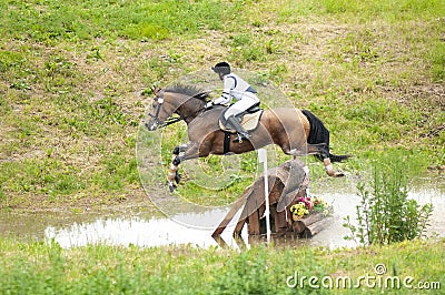 Eventing: equestrian rider jumping over an a log fence water obstacle Stock Photo